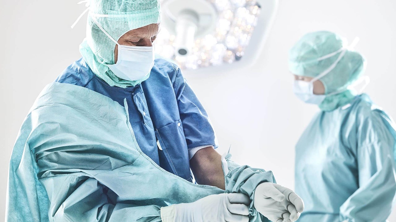 a surgeon and a nurse in an operation room wearing Mölnlycke gowns, gloves, face masks and headwear